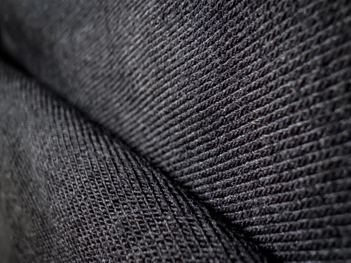 Close-up of a dark charcoal gray merino knit fabric with a diagonal fold showing the texture and weave.