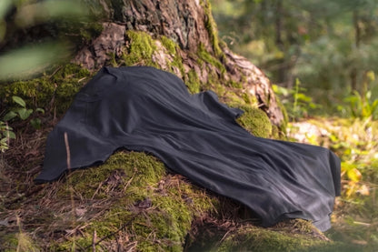 A Charcoal lightweight merino fabric t-shirt is draped over the base of a mossy tree in a forest setting.